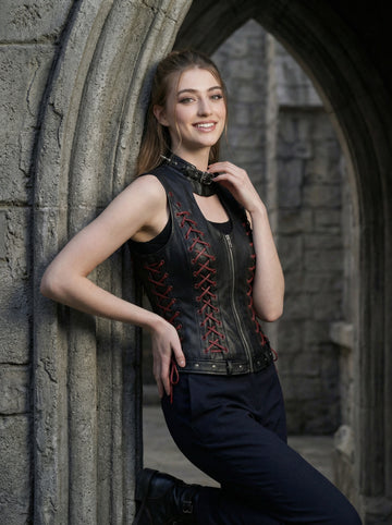 Black gothic leather vest for women with high neck collar, red lace-up side detail, sleeveless fitted corset style, and black pants in stone arch photoshoot