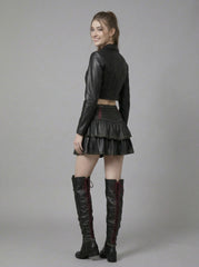 Woman wearing a gothic black leather crop top, mini skirt, and knee-high boots on a gray background